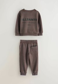 Brūns adīts džemperis ar melnā krāsā uzrakstu "ALLSAINTS LONDON", kombinēts ar atbilstoša stila šaurām sporta biksēm ar kabatu aizmugurē.