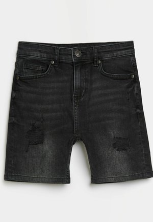 Sorte denimbukser med slidte pletter, frontknap, lynlås, bæltestropper og femlommers design lagt fladt på hvid baggrund.