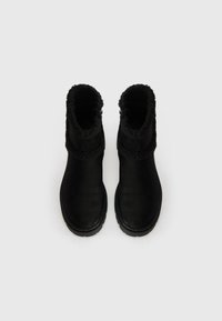 Fekete velúr bokacsizmák texturált szőrme felső résszel, kerek orral és lapos gumitalppal. Az oldalsó részén cipzáros záródással rendelkezik.