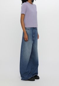 Maglione a maniche corte a coste di un delicato viola abbinato a jeans blu a gamba larga a vita alta. Scarpe piattaforma nere e chunky.
