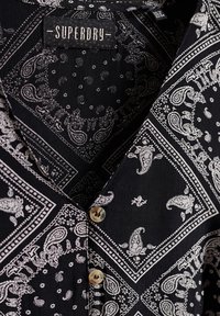 Schwarzes gemustertes Hemd mit weißem Paisleymuster, ausgestattet mit einem Kragen und zwei Knopfverschlüssen, aus leichtem Stoff gefertigt.