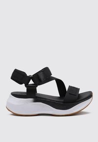 Sandalia negra con correas de tela ajustables y una amplia suela blanca. Presenta una base texturizada y una plantilla suave para mayor comodidad.