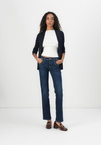 Navy ribbed cardigan over a white fitted top, paired with straight-leg dark denim jeans and brown loafers with gold accents.