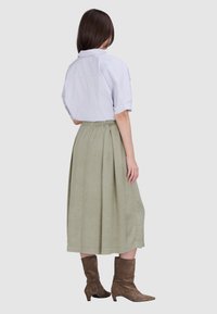 Witte korte mouwen shirt, groene midi plisseerrok en bruine enkellaarzen. Zacht, licht materiaal, casual ontwerp en elastische tailleband.