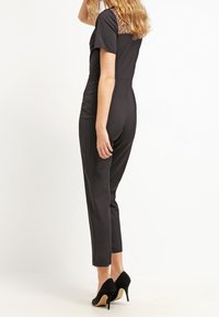 Svart jumpsuit med korta ärmar, texturerad ryggdetalj, slim fit, avsmalnande ben och bärs med svarta högklackade skor.