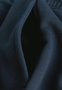 Marineblaue Stoff mit weicher Textur, ausgestattet mit einer Taschenöffnung und einem gesteppten Saum entlang der Kante, der eine glatte Verarbeitung verleiht.
