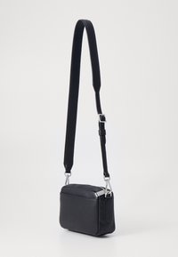 Borsa a tracolla nera in pelle con finitura testurizzata, forma rettangolare, accessori in argento e tracolla regolabile. Presenta una chiusura a zip.
