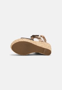 Sandale compensée avec semelle plateforme tressée, brides en cuir beige et noir, et une boucle dorée ajustable, vue du côté inférieur.