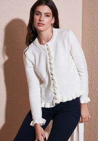 Weißer gestrickter Cardigan mit geripptem Kragen, fransigen Kanten und dekorativem Knopfverschluss. Glatte Textur und taillierte Passform.