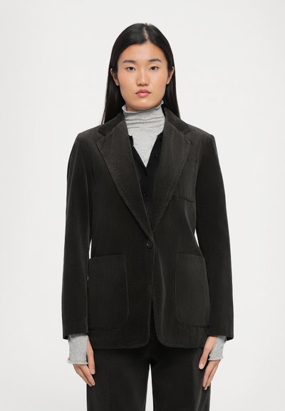 Dark green corduroy blazer with notched lapels, two front pockets, single button closure, worn over a gray turtleneck.