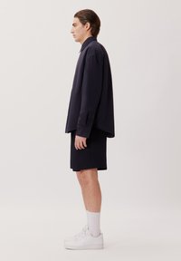 Marine knoopshirt met een losse fit, gecombineerd met knielange donkere shorts en witte sneakers. Glad textuur, minimale ontwerpkenmerken.