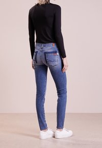 Tight jeans i medelblå denim med bakfickor som har en kontrasterande detalj. Matchat med en svart långärmad topp och vita sneakers.
