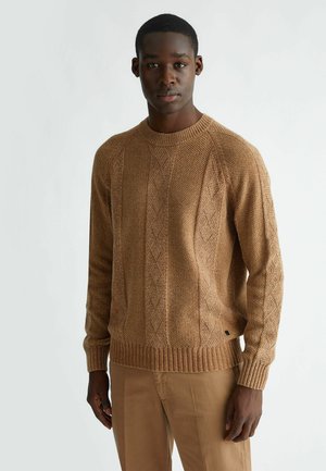 Maglione lavorato a maglia in marrone chiaro con un motivo a treccia testurizzato, scollatura e polsini a coste, e una vestibilità rilassata. Abbinato a pantaloni beige.