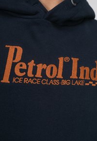 Marineblauwe hoodie met een oranje geborduurd "Petrol Ind" logo en de tekst "ICE RACE CLASS-BIG LAKE". Bevat een verstelbare capuchon en een zachte textuur.