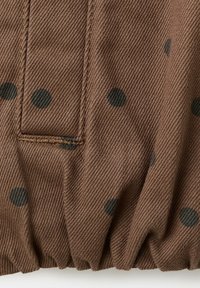 Tela marrón con lunares negros, costura visible y dobladillo elástico fruncido en el borde inferior.