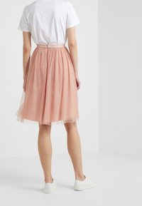 Gonna in tulle rosa con motivo a pois, vita arricciata e design a strati, abbinata a una maglietta bianca semplice e scarpe bianche.
