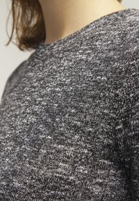 Maglione grigio lavorato a maglia con un motivo testurizzato. Presenta un collo rotondo e un tessuto morbido, mescolando filati scuri e chiari.