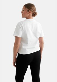 Vit bomullströja med korta ärmar, klassisk rund halsringning och en avslappnad passform, tillsammans med svarta ribbade leggings.