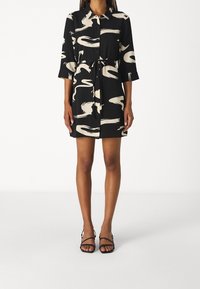 Vestito nero a camicia con motivi astratti color crema, maniche corte e cintura in vita. Abbinato a sandali neri con fasce.