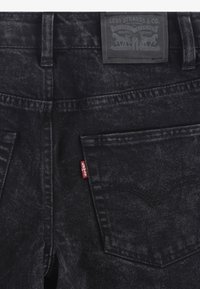 Pantalones vaqueros de mezclilla negra con acabado texturizado, con una etiqueta de cuero de la marca en la parte trasera y una pestaña roja en el bolsillo izquierdo.