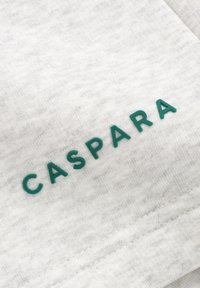 Grått stoff med en myk tekstur som har ordet "CASPARA" i teal, preget på materialet. Minimalistisk design med rene linjer.
