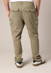 Olijfgroene cargobroek met een tapered fit, voorzien van twee achterzakken met knopen en zijzakken. Gecombineerd met zwart-witte sneakers.