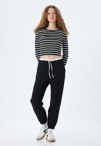 Zwart-wit gestreepte cropped longsleeve top, gecombineerd met zwarte joggingsbroek met een elastische tailleband en boorden, gedragen met witte sneakers.