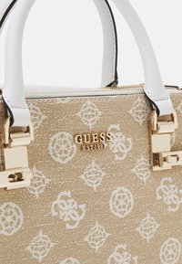 Beige textured handbag with white logo pattern, gold hardware, and white handles. Features a zip closure and a brand logo.