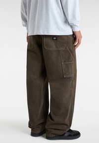Cargo-byxor i mörk olivgrön, med avslappnad passform, framfickor och en bakficka med varumärkesetikett. Materialet verkar hållbart och strukturerat.