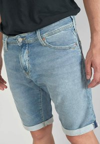 Shorts en denim bleu clair avec des ourlets retroussés, comportant cinq poches, des passants de ceinture et une fermeture à bouton en métal. Texture lisse avec des détails délavés.