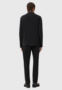 Black suit jacket and pants, smooth fabric, tailored fit, single vent at the back, accented with simple hardware, worn with black shoes.