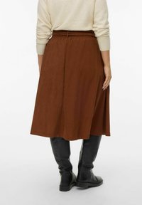 Bruine, knielange rok met een elastische tailleband en een gladde textuur, gecombineerd met hoge zwarte leren laarzen.