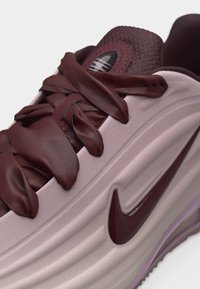 Κοντινό πλάνο ροζ και μπορντό αθλητικού παπουτσιού Nike με χοντρές σατέν κορδόνια, υφασμένη γλώσσα και λογότυπο swoosh στο πλάι πάνω σε μαλακή σόλα.
