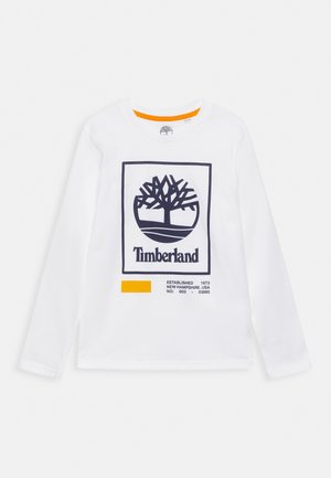 Hvid langærmet skjorte med navymærket Timberland trælogo inden for en firkant og teksten "Established 1973 New Hampshire USA" med en orange rektangulær accent.