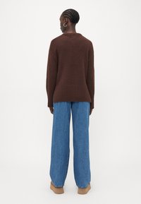Brauner gestrickter Pullover mit geripptem Saum, kombiniert mit weit geschnittenen blauen Jeans. Der Pullover hat eine lockere Passform und ein Rundhals-Design.