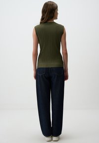 Top senza maniche verde oliva con texture a righe verticali, abbinato a jeans larghi blu scuro e sneakers bianche. Outfit semplice e informale.