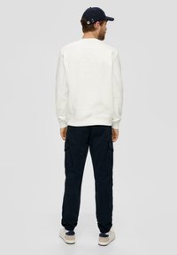 Witte sweatshirt met ronde hals, gecombineerd met donkerblauwe cargobroek met zijzakken, en witte sneakers. De outfit is van achteren bekeken.