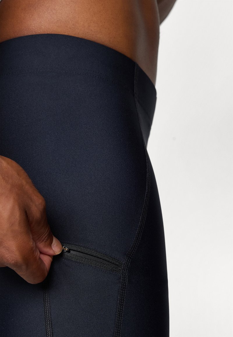 Zwarte sportleggings hebben een gladde textuur, een aansluitend ontwerp en een ritszak aan de zijkant voor opslag.