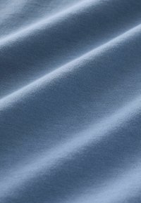Světle modrá látka s jemnou texturou, s jemným žebrováním. Materiál vypadá hladce, s viditelnými záhyby a stíny.