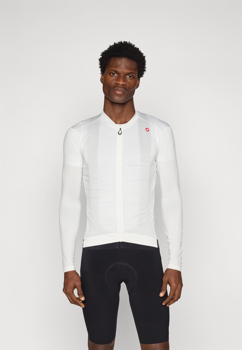 Weißes Langarm-Radsporttrikot mit strukturiertem Design, Reißverschluss vorne und kleinem Logo. Trägt man über schwarzen Radsportshorts.