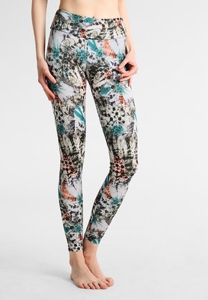 Legginsy o dopasowanym kroju z kolorowymi abstrakcyjnymi wzorami kwiatowymi i piórami w kolorach morskim, pomarańczowym, czarnym i białym, noszone przez osobę stojącą boso.
