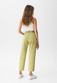 Pantalon vert clair taille haute à coupe décontractée, jambes droites et ourlets effilochés, associé à des baskets blanches et un haut sans manches.