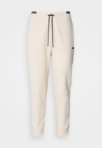 Cremfarbene Jogginghosen mit einem elastischen Bund und Kordelzug, schwarzen Akzenten, schmal zulaufenden Beinen und seitlichen Taschen.