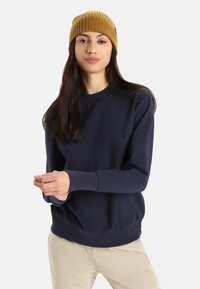 Navy sweatshirt with ribbed cuffs and hem, paired with a yellow ribbed knit beanie. Smooth fabric, relaxed fit, minimal design.