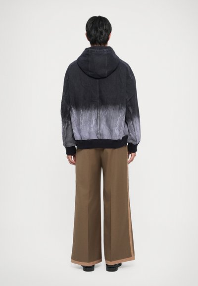 Black and gray dip-dyed hoodie with a textured finish, featuring a hood and ribbed cuffs, paired with wide-legged brown trousers.