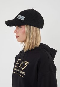 Cappello da baseball in pile nero con visiera curva e un patch riflettente con il logo EA sulla parte anteriore. Il design presenta una superficie testurizzata.