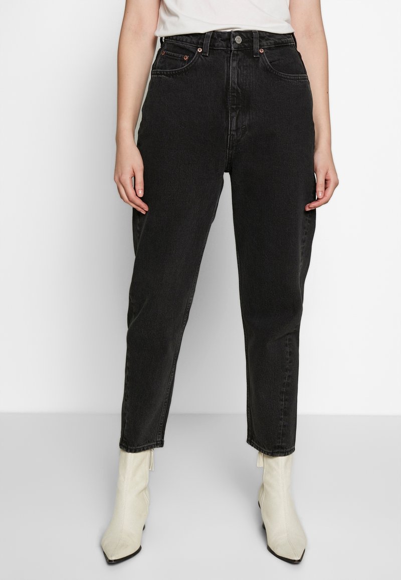 Jeans neri a vita alta realizzati in denim, con taglio dritto, cinque tasche e dettagli in bottone di rame, abbinati a stivaletti bianchi alla caviglia.