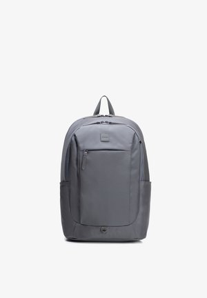 Šedý batoh s přední kapsou na zip, bočními kapsami, polstrovaným madlem a dvěma kapsami na zip, zobrazený na bílém pozadí.