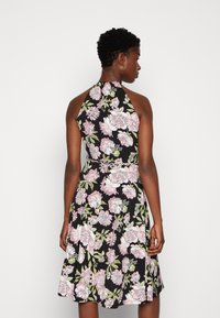Vestido halter floral em tecido preto. Apresenta grandes flores rosas e brancas com folhas verdes. Saia ampla e design de cintura ajustada.