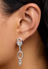 Silberne Ohrhänger mit einem schlossförmigen Ohrstecker und verbundenen kreisförmigen Ketten, die eine polierte Oberfläche und ein schlankes Design präsentieren.